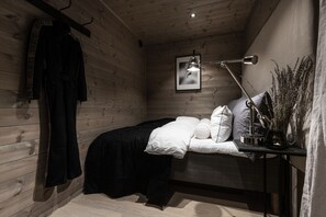 Un dormitorio con cama, perchero, escritorio con lámpara y un cuadro en la pared.