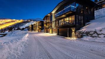 A snow-covered road leading to a modern building with large windows and a balcony.
