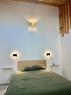 Ein Schlafzimmer mit einem hölzernen Kopfteil, zwei Nachttischen mit Wandlampen und einem Bett mit grüner Bettdecke.