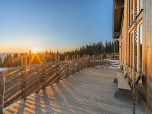 A wooden deck with a view of a forest and a building with large windows.