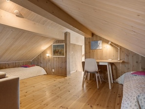 An attic bedroom with wooden walls and floors, a desk with a chair, and two beds. - Ski cabin in Hafjell (Øyer)