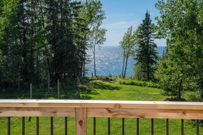A wooden deck with a view of a grassy area and trees. - Owl's Nest: Sunlit South Shore Lakefront Home | Stairs Down to Lakeshore (Herbster)
