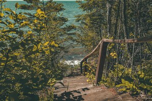 A wooden staircase leading to a beach with dense foliage on either side. - Owl's Nest: Sunlit South Shore Lakefront Home | Stairs Down to Lakeshore (Herbster)