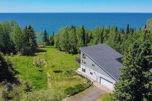 Une maison à deux étages avec un garage, entourée d’une pelouse bien entretenue et d’arbres, et offrant une vue sur une vaste étendue d’eau.