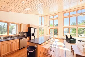 Une cuisine spacieuse avec des meubles en bois, un grand îlot central doté de tabourets de bar et un coin repas offrant une vue sur l’extérieur.