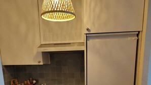 Een compacte keuken met een fornuis, oven en koelkast, een hanglamp en een betegelde spatwand.