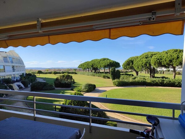 A balcony with a view of a well-maintained garden, a white building, and a clear sky.