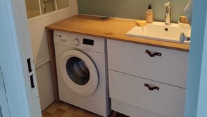 Een praktische badkamer met een wasmachine, een douchecabine, een houten kastje, een spiegel en een wastafel.