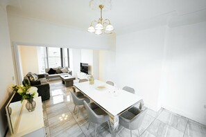 A modern living room with a sofa, a dining table with chairs, a TV, and a vase with flowers. - Upscale 3 BDR Modern Home in Anfield Liverpool (Liverpool)