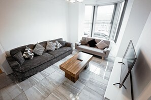 Un salon moderne avec un canapé gris, un canapé blanc, une table basse en bois et un téléviseur à écran plat.