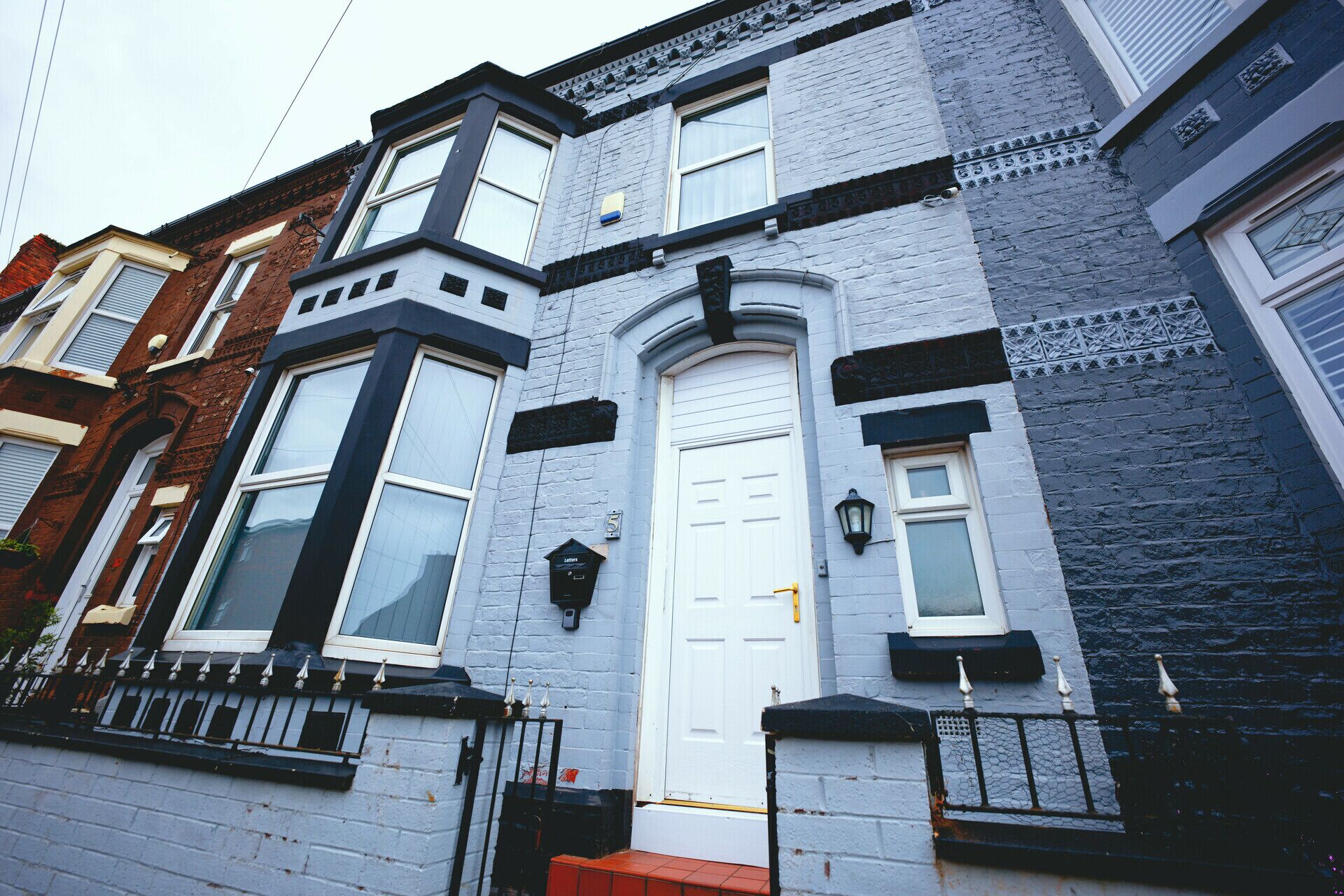 A two-story townhouse with a white front door, bay windows, and a black metal fence.