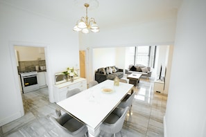 A modern kitchen with a central island, a dining area with a white table, and a living room with a sofa and a TV. - Upscale 3 BDR Modern Home in Anfield Liverpool (Liverpool)