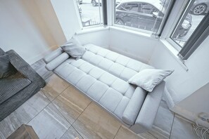 A light grey sofa with a cushion, positioned in a corner with a view of the street through a window. - Upscale 3 BDR Modern Home in Anfield Liverpool (Liverpool)