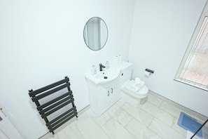 A bathroom with a white sink, toilet, and a mirror above the sink. There is a towel rack to the left and a window with blinds to the right. - Upscale 3 BDR Modern Home in Anfield Liverpool (Liverpool)