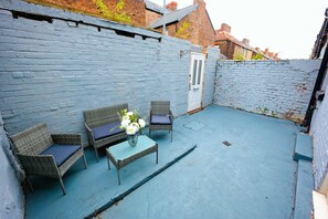 A small patio area with wicker furniture, a table, and a vase of flowers. - Upscale 3 BDR Modern Home in Anfield Liverpool (Liverpool)