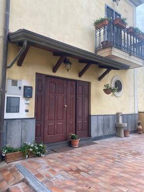 A building with a large wooden door, a small balcony with potted plants, and a stone fountain. - Relax Pompeii Studio (Pompei)
