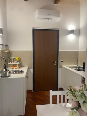 A compact kitchenette with a stove, kettle, and storage shelves, a wooden door, and a white sink with a faucet. - Relax Pompeii Studio (Pompei)