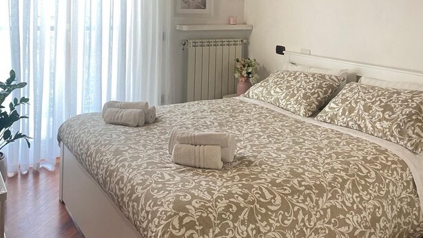 Ein Schlafzimmer mit Holzboden, einem großen Bett mit gemusterten Textilien, einem Heizkörper und einem Fenster mit Vorhängen.