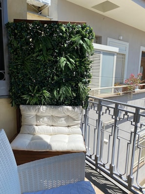 A balcony with a white cushioned bench, a metal railing, and a green leafy wall. - Relax Pompeii Studio (Pompei)
