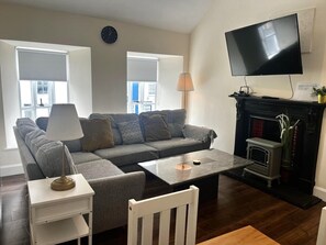 Ein Wohnzimmer mit einer Couch, einem Couchtisch, einem Fernseher, einem Kamin und einer Uhr.