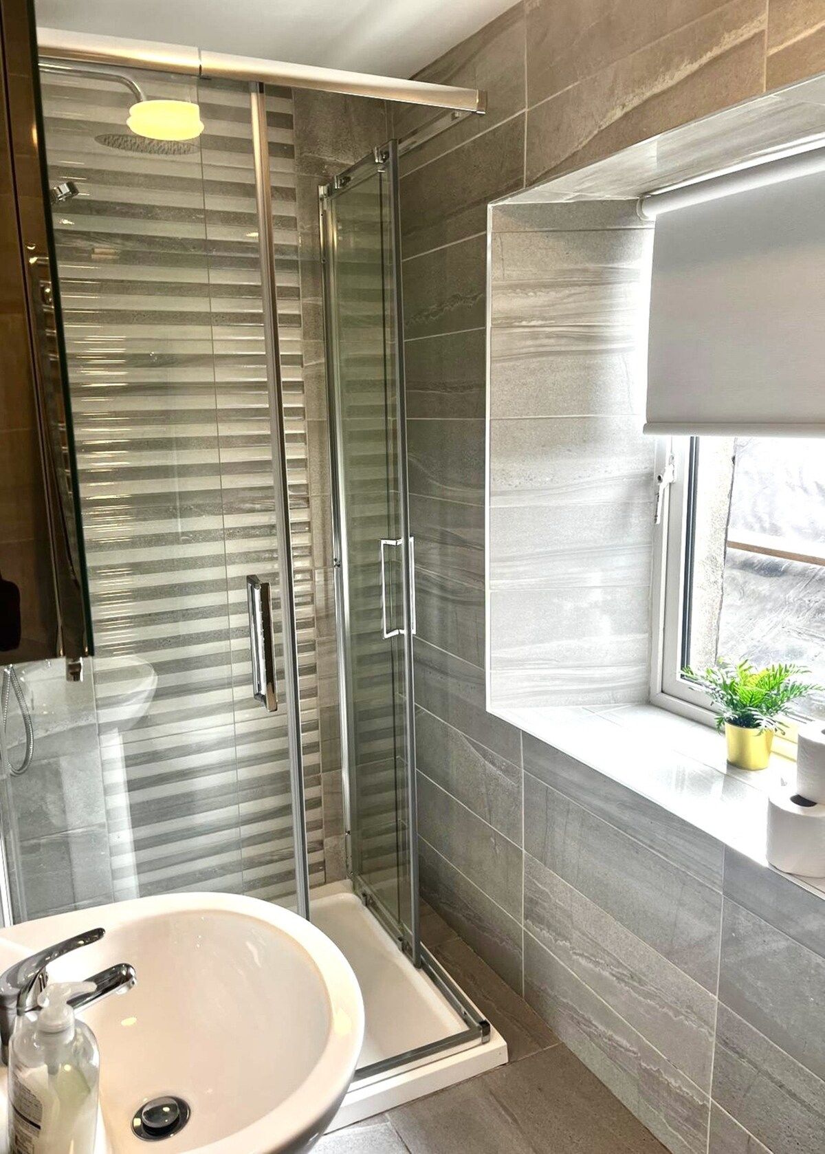 A modern bathroom with a glass-enclosed shower, a sink with a mirror, and a window with a view.