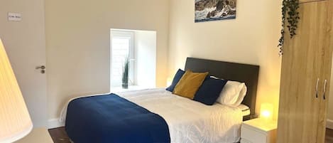 A bedroom with a bed, bedside tables, a wardrobe, a window, and a painting on the wall.
