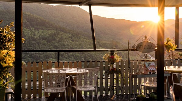 A terrace with a view of a forested mountain range, a welcome sign, and outdoor seating.