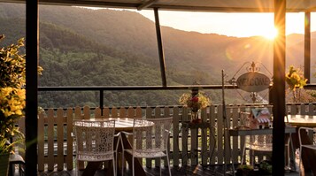 A terrace with a view of a forested mountain range, a welcome sign, and outdoor seating.