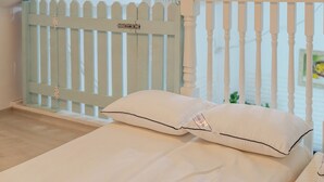 Uma cama com dois travesseiros, um corrimão branco e vista para uma cerca azul clara.