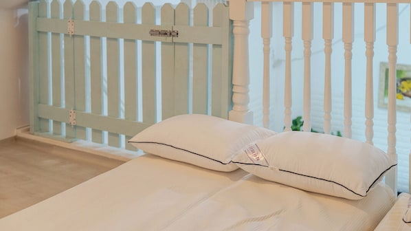 A bed with two pillows, a white railing, and a view of a light blue fence. - Gapyeong Darin Pension (Gapyeong)