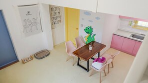 A child's room with a wooden table, pink chairs, a dinosaur wall decal, and a kitchen area with pink cabinets. - Gapyeong Darin Pension (Gapyeong)