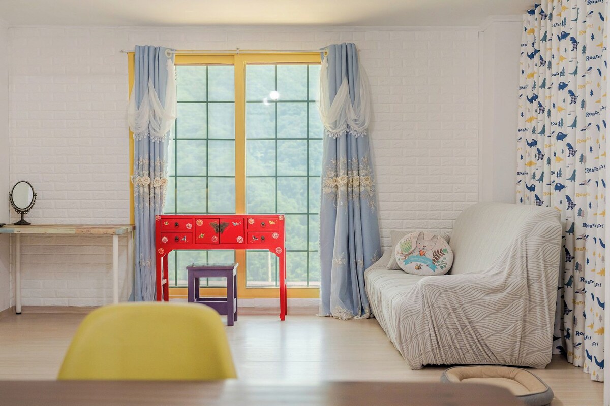 A room with a window, a red table, a chair, and a bed.