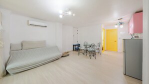 Quarto com cama, mesa de jantar com cadeiras, cozinha equipada com frigorífico e uma porta amarela.