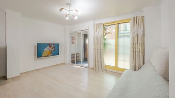 Un salón amplio con una televisión de pantalla plana, un sofá, una puerta corrediza de vidrio y una lámpara en el techo.
