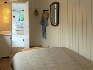 Ein Schlafzimmer mit einem Bett, einem Spiegel, einem Kleiderhaken und einem Korbwäscheschrank.