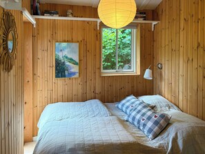 Ein Zimmer mit Holzwänden, einem Bett, einem Fenster mit Blick auf Grünflächen, einem Gemälde und einer Pendelleuchte.