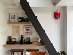 Eine Küche mit einer schwarzen Treppe, einer Kaffeemaschine, einem Wasserkocher und einer roten Maske an der Wand.