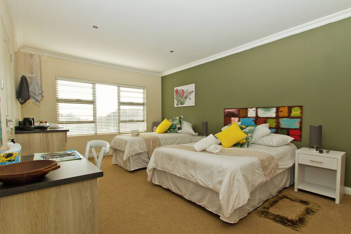 A hotel room with two beds, a small desk, a chair, and a window with blinds.