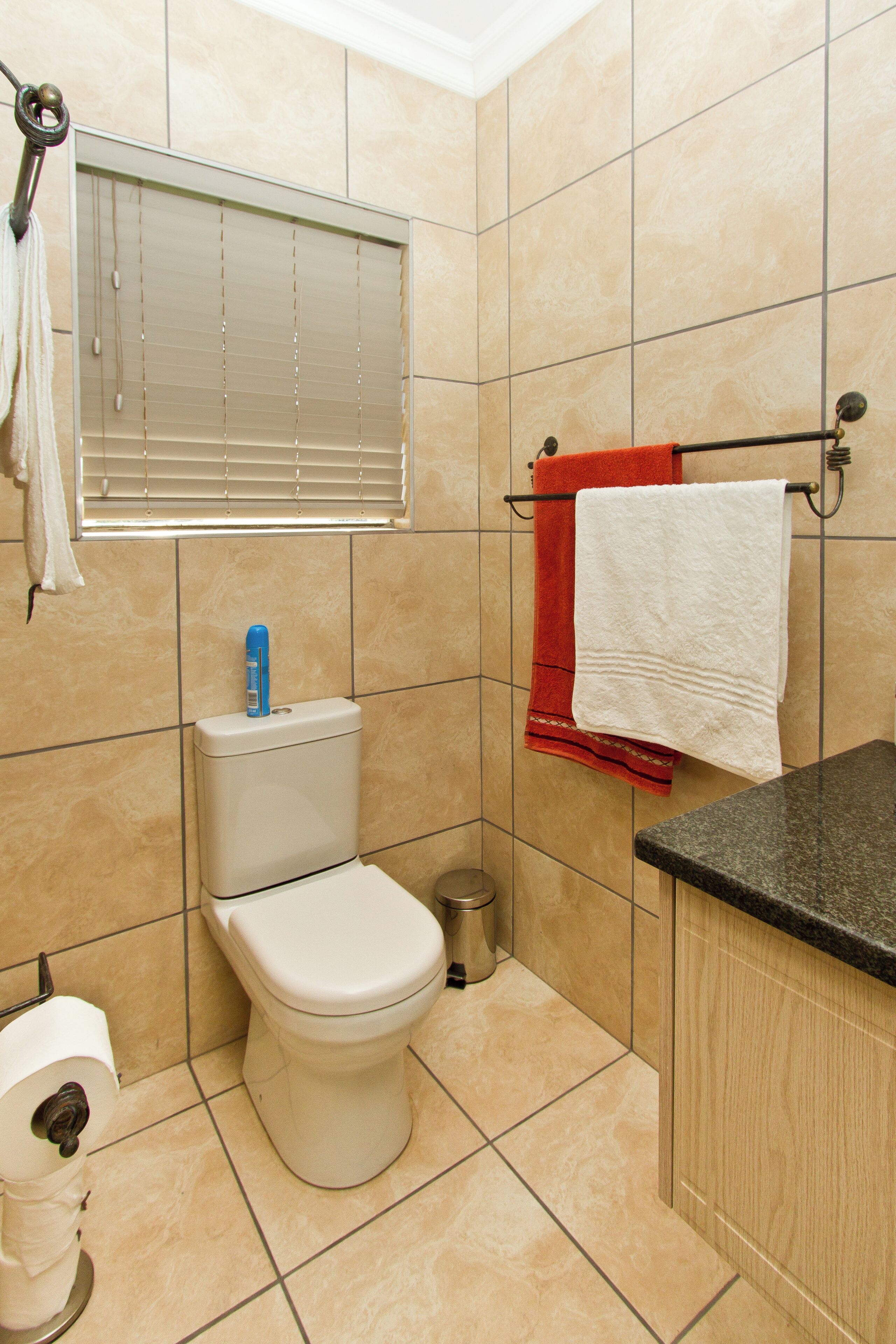 A bathroom with a toilet, a bidet, a towel rack with towels, and a window with blinds.