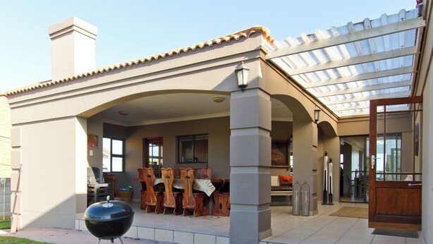 Un patio cubierto con una parrilla, mobiliario exterior y vistas al interior.