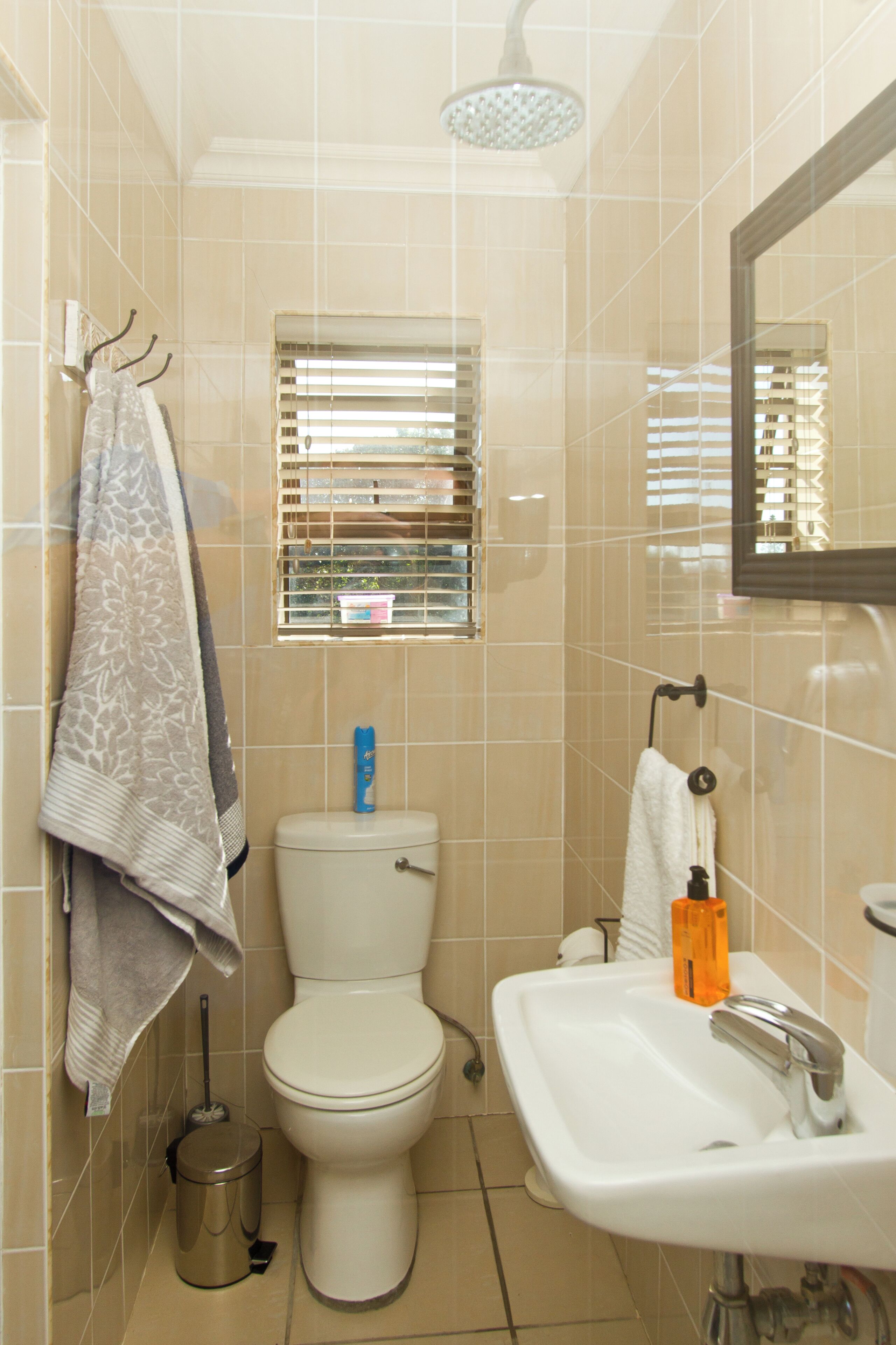 A bathroom with a toilet, sink, shower, and a window with blinds.