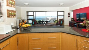 A kitchen with wooden cabinets, a black countertop, and a view of the sea through large windows.