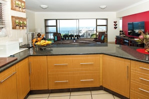 Una cocina con armarios de madera, encimera negra y vista al mar a través de amplias ventanas.