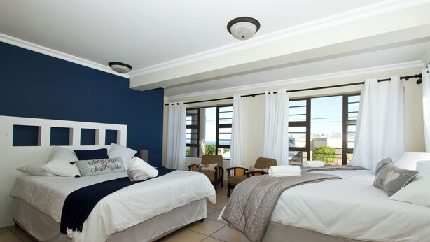 A hotel room with two beds, a small table, chairs, and large windows.