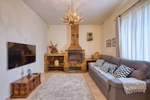 Ein Wohnzimmer mit Kamin aus Stein, einer Couch, einem Fernseher und einer Chandelüster.