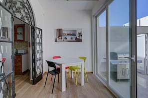 A dining area with a round table and four chairs, a kitchen with cabinets and a toaster, and a sliding glass door leading to an outdoor grill area. - Luxury 4BR Villa Terrace & BBQ in St Julian’s (San Ġiljan)