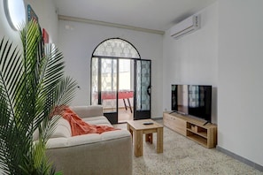 A living room with a sofa, TV stand, and a door leading to a balcony. - Luxury 4BR Villa Terrace & BBQ in St Julian’s (San Ġiljan)