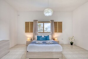 Une chambre à coucher avec un lit, des lampes de chevet, une fenêtre avec des volets, un luminaire suspendu et une plante en pot.