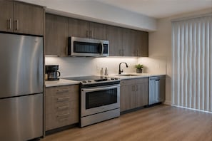 A modern kitchen with stainless steel appliances, wooden cabinets, and a built-in microwave. - Cendelle City Suites (Toronto)