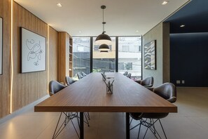 A conference room with a long wooden table, black chairs, a pendant light, and artwork on the walls. - Charlie Murat Vila Madalena (São Paulo)